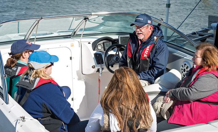 Senior male at the wheel of a vessel speaking with four females while out at in open waters.