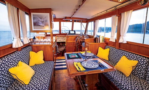 Main saloon of a vessel featuring yellow throw pillows and blue and white padded couches.