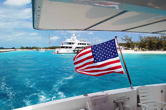 Flying the American flag off the back of a boat, with teal blue water and several other boats anchored in the same area.