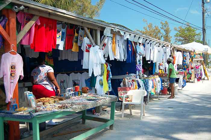 An outdoor market featuring many colorful tshirts and a table of trinkets for sale