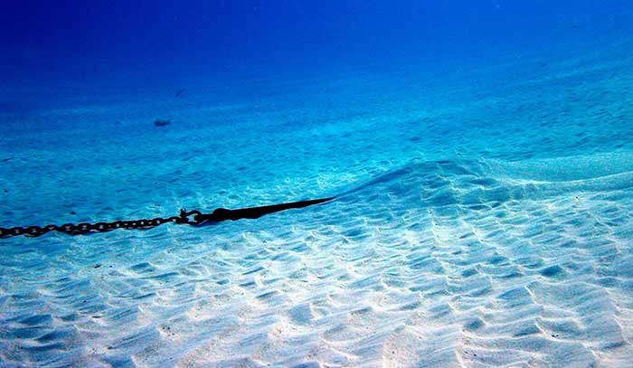 An underwater view of the ocean's sandy floor with a boat anchor buried in the sand.