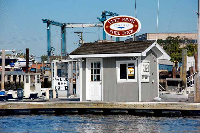A small grey building on a dock with signage overhead that reads "YACHT HAVEN FUEL DOCK" with a Valtect fuel sign in the window.