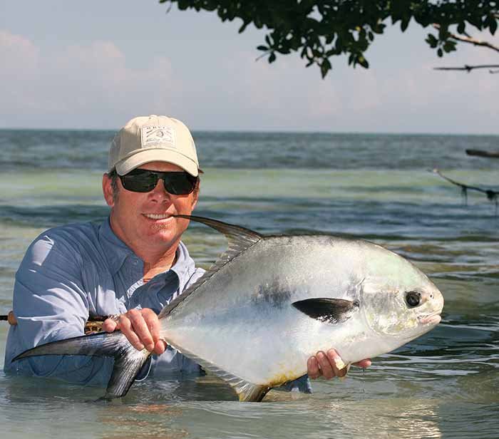 A man stands in clear blue waters and holds up a fish he caught