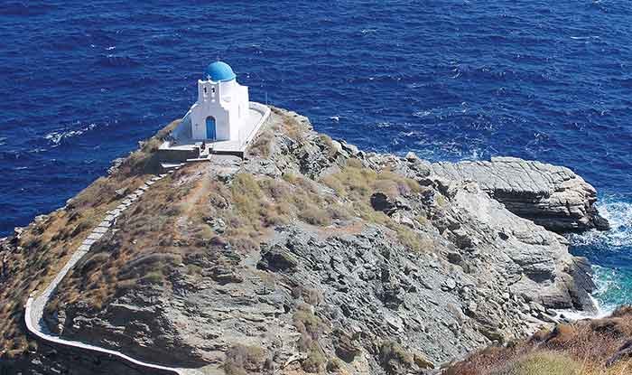 A white church with blue roof overlooks the ocean on a cliff