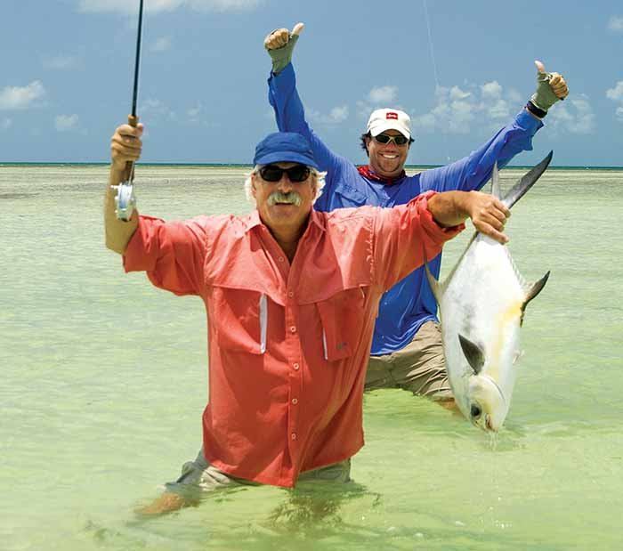 Two men Fishing in the Florida Keys -- one man holding up a fish they caught while the other gives two thumbs-up.