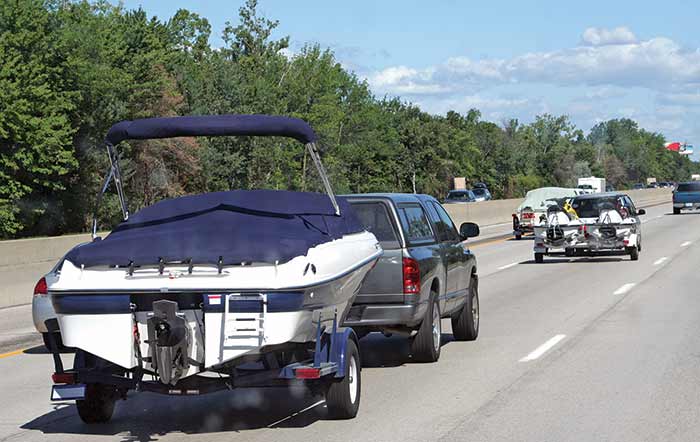 Two pickup trucks each towing a boat behind them cruising down a highway.