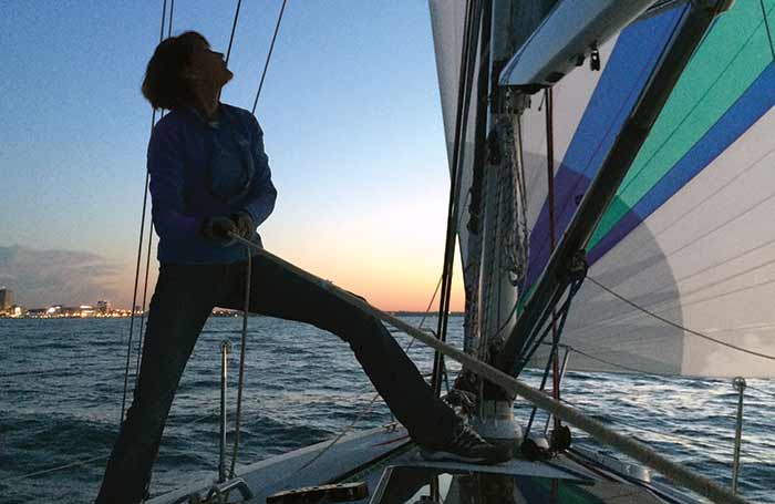 A woman pulls at a rope onboard a sailboat and looks up at the sails