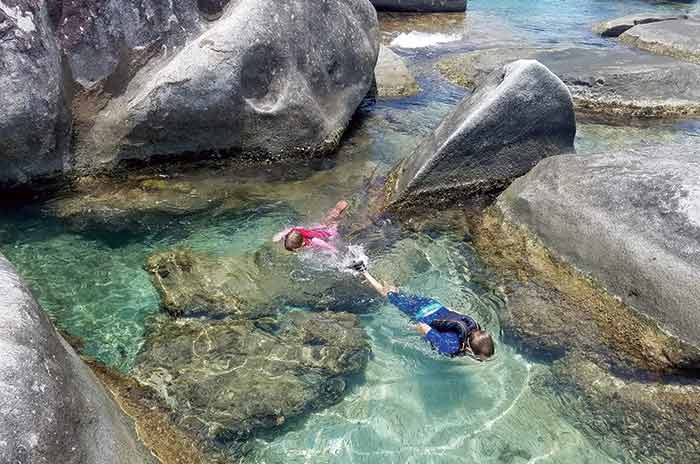Two people swimming in clear water surrounded by large rocks