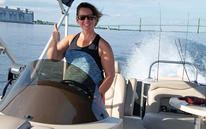 A woman wearing sunglasses smiles from the helm of a powerboat giving a thumbs up