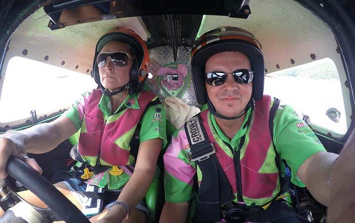 A man and a woman in the cockpit of a boat, both wearing a pink and green uniform.