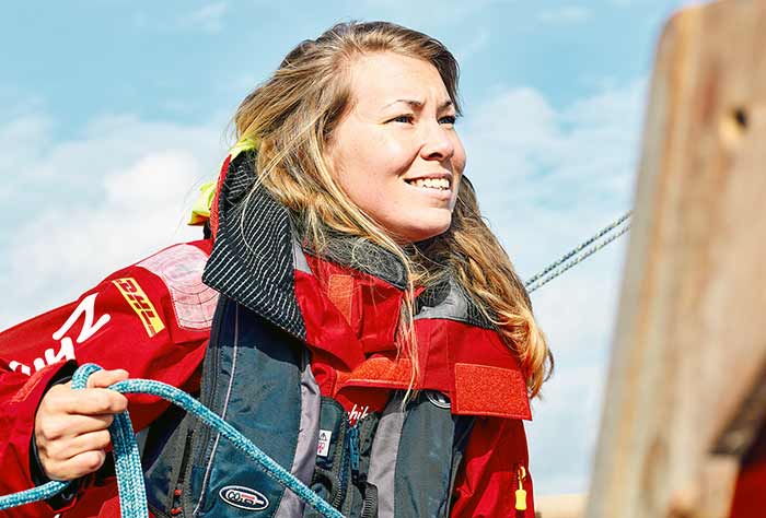 A woman in a red sailing jacket smiles as she holds blue rope in her hands.