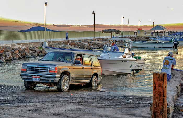 SUV backing down boat ramp into the water with large powerboat in tow