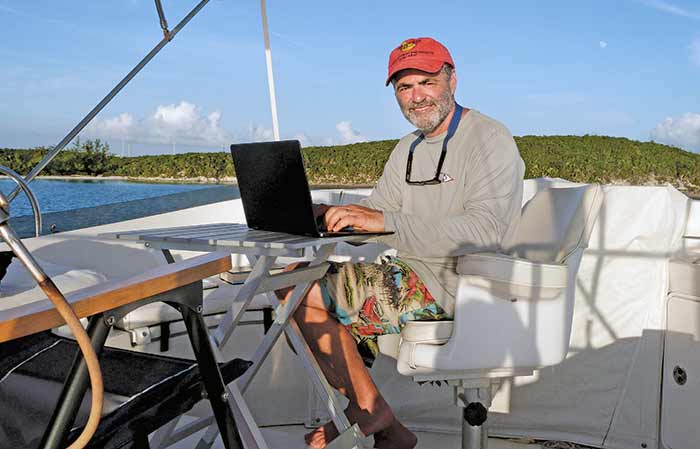 Man sitting at a small table on the deck of a boat working on a laptop computer