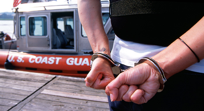 Closeup of hands in handcuffs with US Coast Guard boat in background