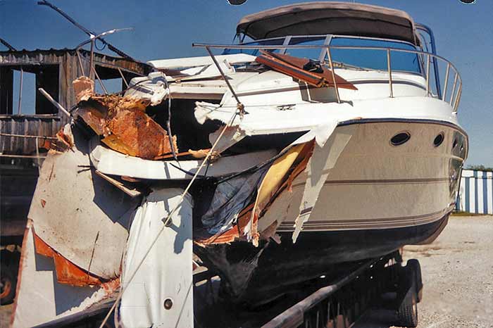 Aftermath of a boat collision with major damage to the stern of  a powerboat sitting on a boat trailer