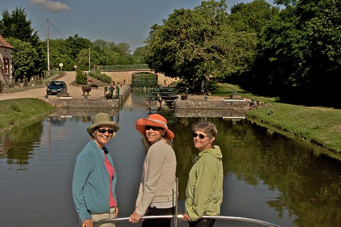 Three women sitting on the bow of a barge approaching a lock as they cruise the canals in Frrance