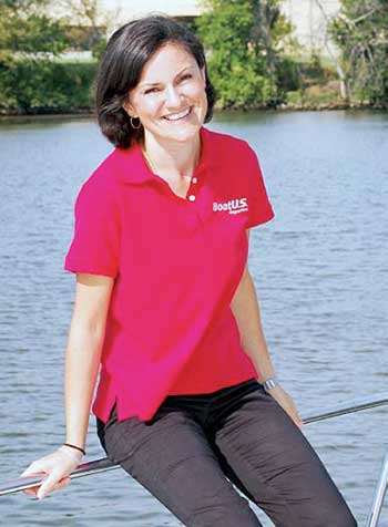 White woman with short dark hair sits on bow of boat in red polo shirt smiling
