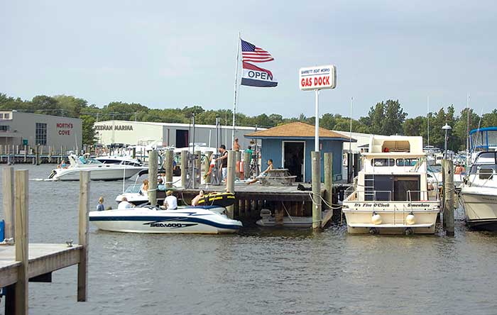 Small powerboat with 4 people aboard docked in front of busy boat fueling station
