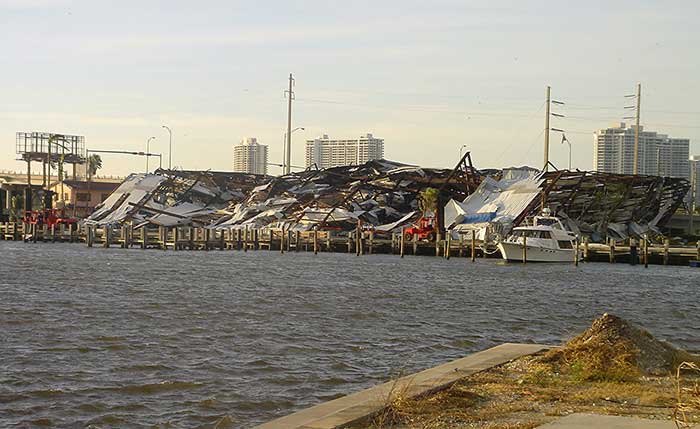 The remnants of a collapsed marina on shore with a white powerboat in the forefront on the water