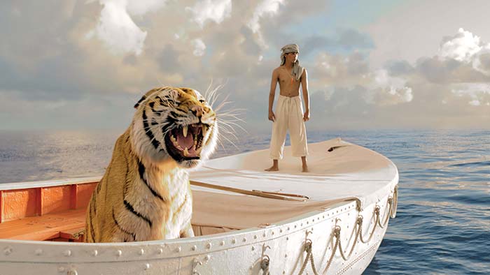 Tiger in a rowboat with young boy standing on the bow; scene from the movie Life of Pi