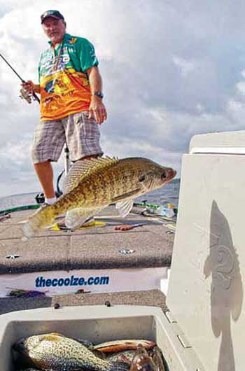 Man holding a fishing rod with his crappie catch over a cooler full of crappie fish