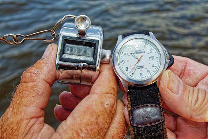 Holding a counter on the left side and holding a watch on the right side with water in the background