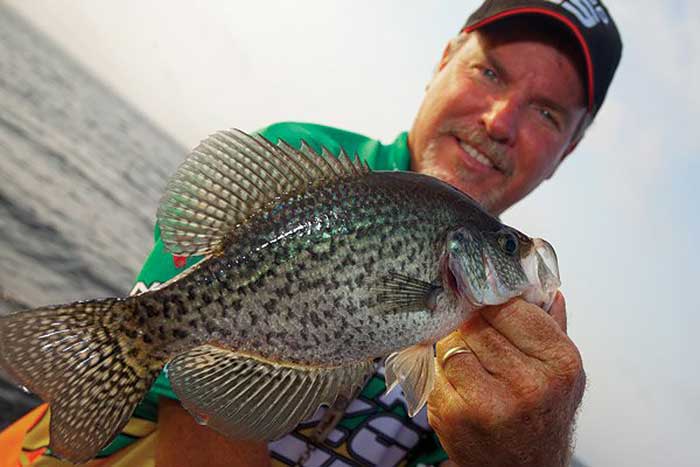 Man hoding a crappie fish in one hand with water in the background