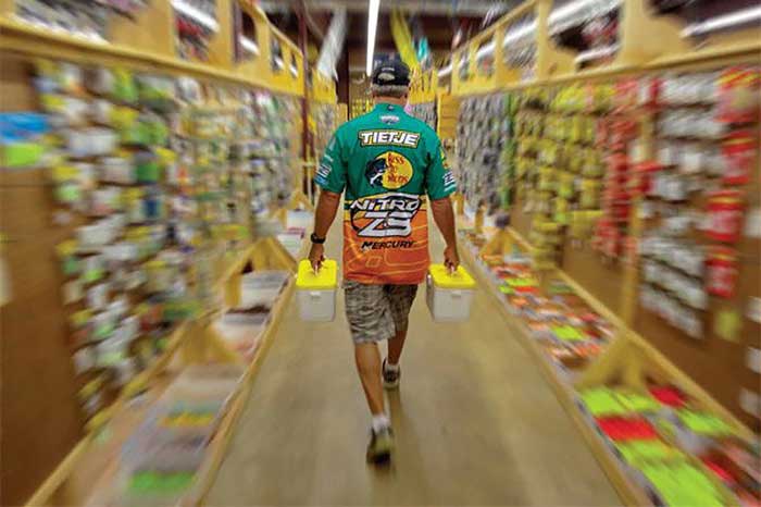 Man walking down the aisel of a fishing supply store holding a plastic container in each hand