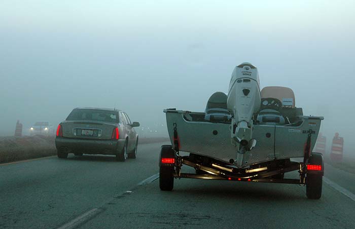 Towing a small powerboat on a trailer with trailer lights visible on a foggy roadway