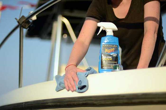 Person with microfiber cloth in hand wiping down boat hull with Quik Wax spray bottle on the end of the boat hull