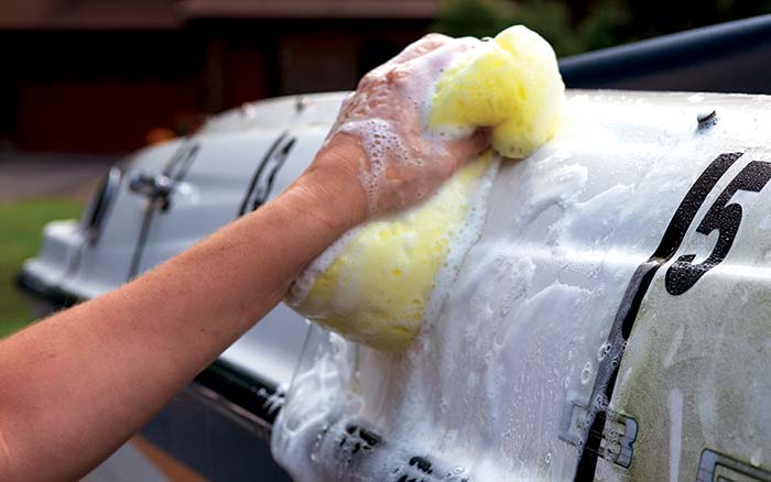 Cleaning a boat hull with a yellow sponge filled with soap and water