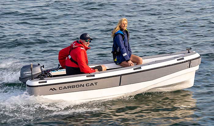 Man holding the tiller of a small Carbon Cat boat with woman sitting in front of him while crusing along