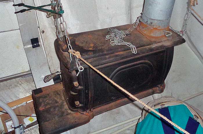 Wood-burning stove suspended by chains, being used as a boat heater