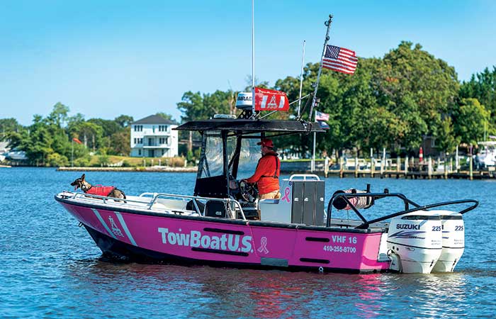 Man with dog on bow cruising down a lake in a TowBoatUS vessel painted pink