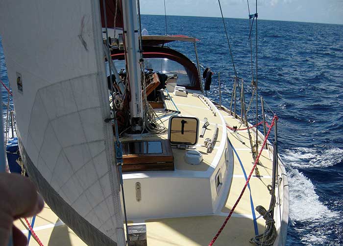 Close-up from the stern of a sailboat with sail fully raised sailing along through the blue water