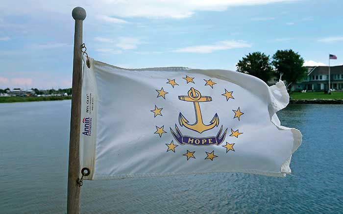 The word : “Hope,” emblazoned on the Rhode Island flag as it flys on a flag pole over the water