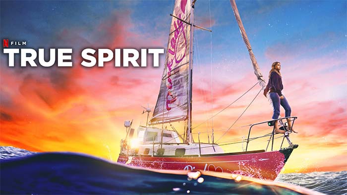 Movie poster for the Netflix film "True Spirit" with girl standing barefoot on the bow of a red sailboat with a coloful sunset sky  over blue water in the background