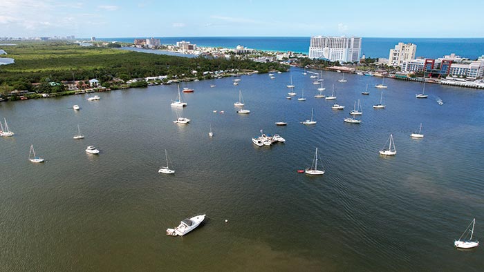 Aerial view of lots of different types of boats moored on a lake with large buildings and coastline in the background
