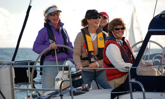 A group of four women smiling  and laughing aboard a sailboat out on the water