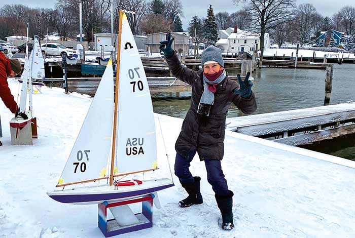 Woman standing next to a radio-controlled sailboat on a blue cinder block in the snow