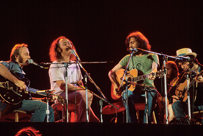 Crosby, Stills, Nash and Young in their early years in front of a black backdrop during a concert