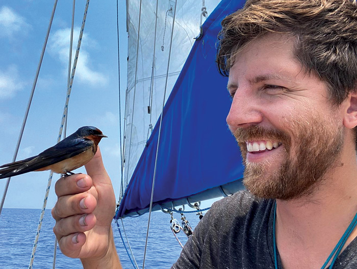 Middle-aged man with a beard holding a little blue bird while on a boat out at sea
