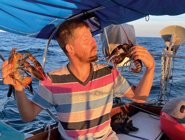 Middle-aged male wearing a striped shirt holding two lobsters on a boat out at sea