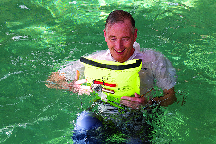 Senior adult male  holding a bright yellow inflatable life jacket in a pool 