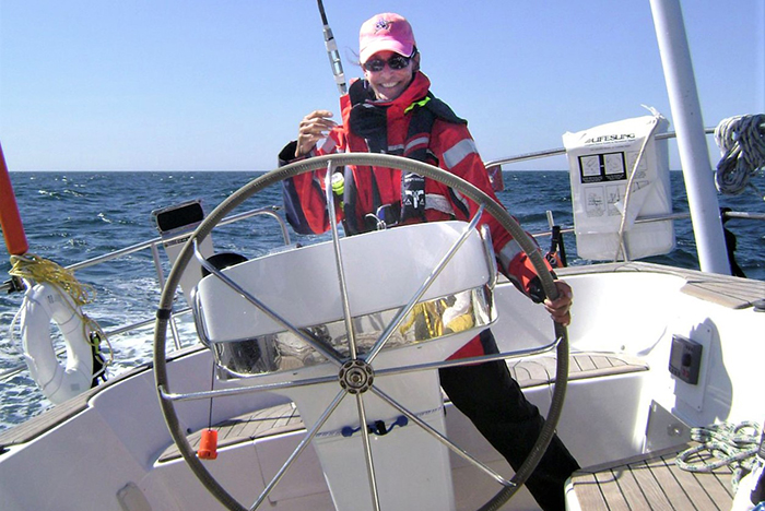 Middle-aged Caucasian female wearing pink baseball hat and red jacket steering a vessel in the open waters on a sunny day