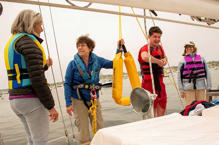 Three women and a teenaged boy learning the ropes aboard a sailboat on the water