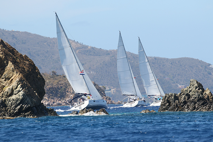 Three white sailboats in the water navigating two large rocks.
