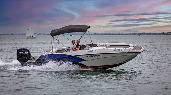 White and blue speedboat with a gray canopy cruising at sunset