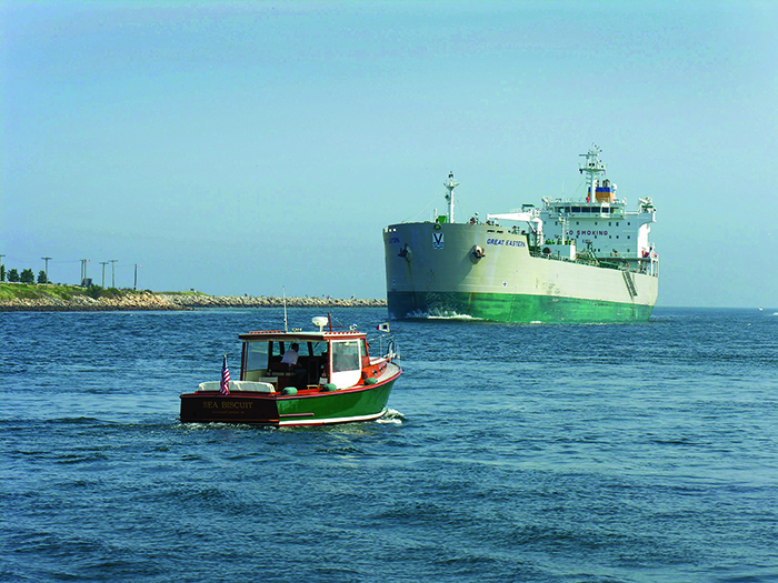 A massive white and green tanker passing by a smaller boat on the Cape Cod Canal.