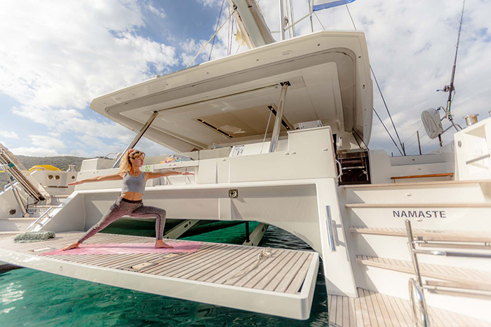 Blonde adult female in black stretch pants doing yoga on the deck of a large white yacht